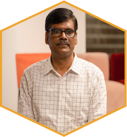 P. R. Sundar, seated, wearing glasses and a light checked shirt.