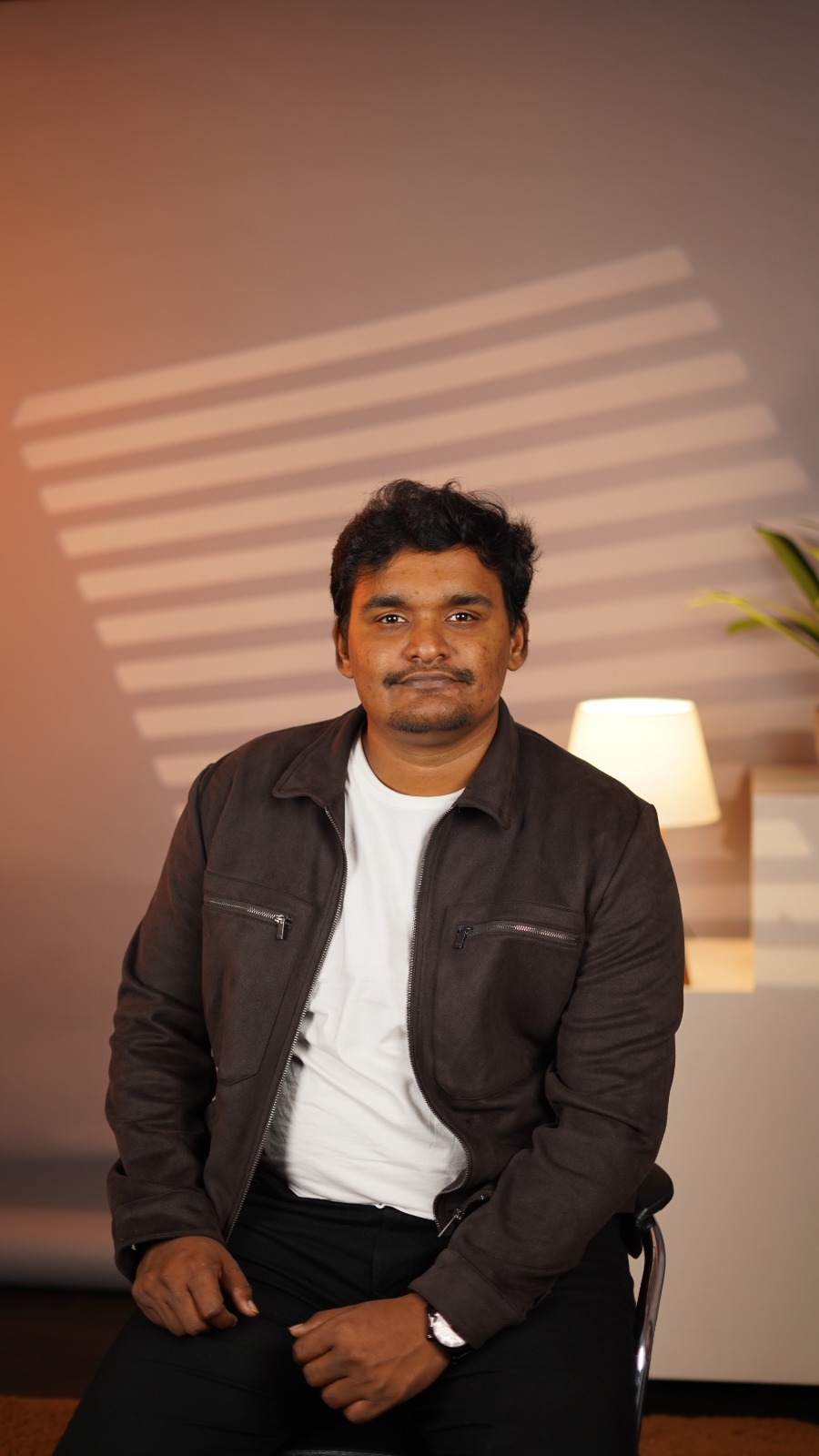 Karthick Aravindan seated with his hands resting together, wearing a dark jacket over a white t-shirt.