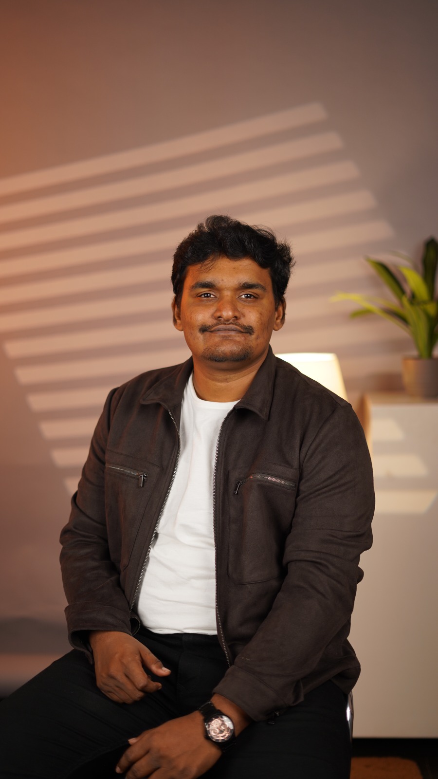 Karthick Aravindan, seated and looking at the camera, in a dark jacket and white t-shirt.